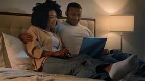Happy family African American married couple husband man and wife woman on bed at night evening browsing net laptop using computer talking shopping app in internet choose film movie in online service - Powered by Shutterstock - Get 15% off with code: PIKWIZARD15