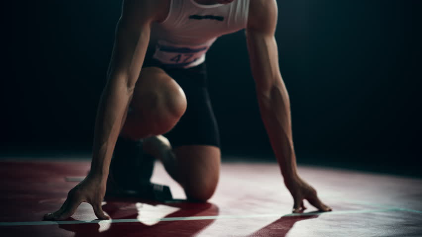 Strong Young Man Starting a Race From Track Starting Blocks Position on a Dark Stadium in the Evening. Cinematic Portrait of a Fit Male Sprint Runner Participating in a Competition Royalty-Free Stock Footage #1110269905