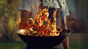 Chef Stir Frying Vegetables in a Flaming Wok in an Outdoors Kitchen. Person Cooking Food Using a Flambe Technique, Igniting Hot Oil and Alcohol in a Pan. Close Up Super Slow Motion Footage - Powered by Shutterstock - Get 15% off with code: PIKWIZARD15