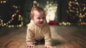 Cute little happy baby crawls at decorated background on camera at Christmas Eve. Family Spend Winter Evening at Home. Child wearing knitted sweater smile search for presents. Happy new year Christmas - Powered by Shutterstock - Get 15% off with code: PIKWIZARD15
