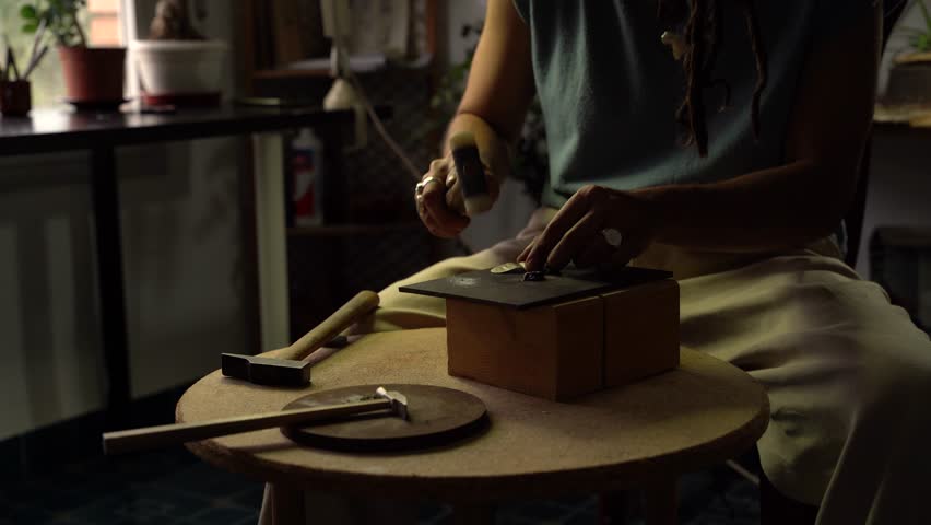 Unrecognizable person hammering a precious stone on a steel plate in the making of a jewel.