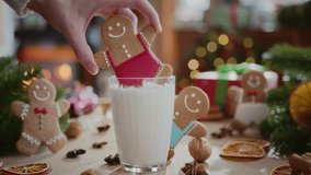 cozy composition of christmas decoration in the morning light. woman hand dips gingerbread man cookie in glass of warm milk on table with presents and burning fireplace on background - Powered by Shutterstock - Get 15% off with code: PIKWIZARD15