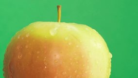 A ripe apple in a raindrop rotates on a green background. Delicious apples