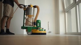 A man polishes wooden floor near the window using big grinding machine. Slow - motion video