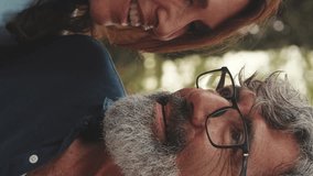 Vertical video, Close up, happy retired couple sitting in the park holding hands and smiling resting on the grass in the park in autumn