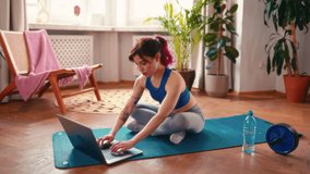Young Asian woman with tattoos in sportswear exercising at home in the living room on a rubber mat with a laptop on video lessons. Sports, yoga and active lifestyle.