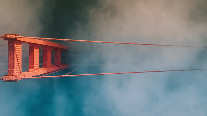 Heavy fog cloud flowing under Golden Gate Bridge aerial view 4K. Cinematic red construction of Golden Gate Bridge in San Francisco on misty day. Top down view on architecture landmark California USA