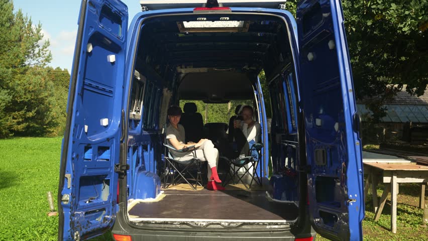 Young couple sits in their van and drinks morning coffee. Man and woman discuses about their project and upcoming tasks in the van build. | Shutterstock HD Video #1110290843