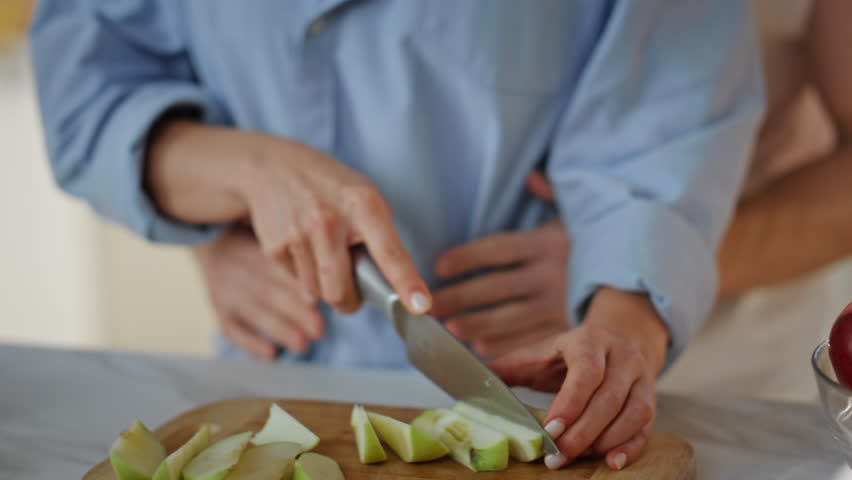 Affectionate couple preparing food at home kitchen close up. Beautiful woman slicing fresh apple for fruit salad. Tender man hugging happy wife cooking healthy breakfast. Young family weekend morning. Royalty-Free Stock Footage #1110294241