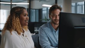 Happy young man and mid adult woman talking and gesturing while using computer in office