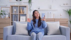 Happy young asian woman relaxing at home. Female smiling and talking chat with friend sitting on sofa and holding mobile smartphone. Girl using video call to close friend