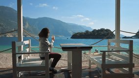 Woman drinking coffee near the sea. 4k video footage in slow motion