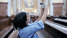 Young beautiful hispanic woman visiting church recording with smartphone at St. Karl Borromäus church