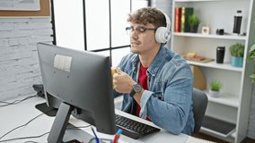 Young hispanic man working at the office, portrait of a professional in a power breakfast, drinking coffee, using computer, wearing headphones, and having video calls on the internet