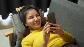 asian women are Cute and beautiful women playing with a mobile phone, chatting, and watching movies online while relaxing on the sofa at home during the holidays.