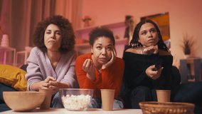 Three relaxed women friends watching boring TV show and eating popcorn, pastime