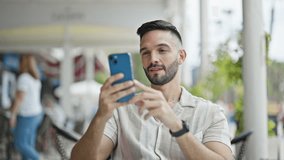 Young hispanic man smiling confident having video call at coffee shop terrace