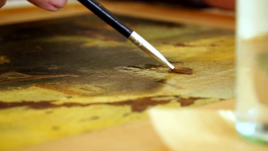 Art restorer applies cleaning fluid to painting with paint brush and removes dirt with cotton wool. Close up of artist at work. Creative, artistic oil painting  in 4k