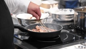 Close-up view of chef cooking rack of lamb in hot frying pan on restaurant kitchen. Soft focus. Real time handheld video. Preparing food theme.