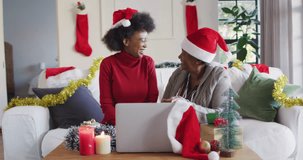 Happy african american mother and adult daughter in santa hats on christmas video call, slow motion. Christmas, communication, laptop, family, togetherness and celebration, unaltered.
