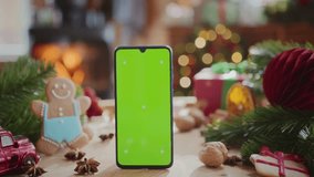 smartphone with green screen chroma key display with motion trackers on table with fir tree branches, gingerbread men and christmas decoration. burning fireplace and flashing lights on background - Powered by Shutterstock - Get 15% off with code: PIKWIZARD15