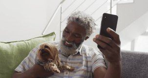 Animation of social media text and icons over senior african american man with dog at home. Global social media, digital interface, computing and data processing concept digitally generated video.