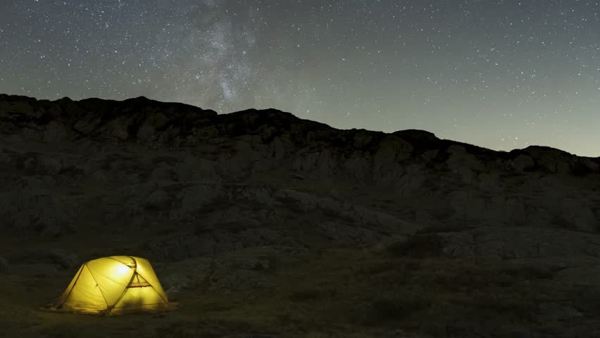 Milky Way over Yellow Glowing Tent. Starry Sky. Night Landscape. Time Lapse