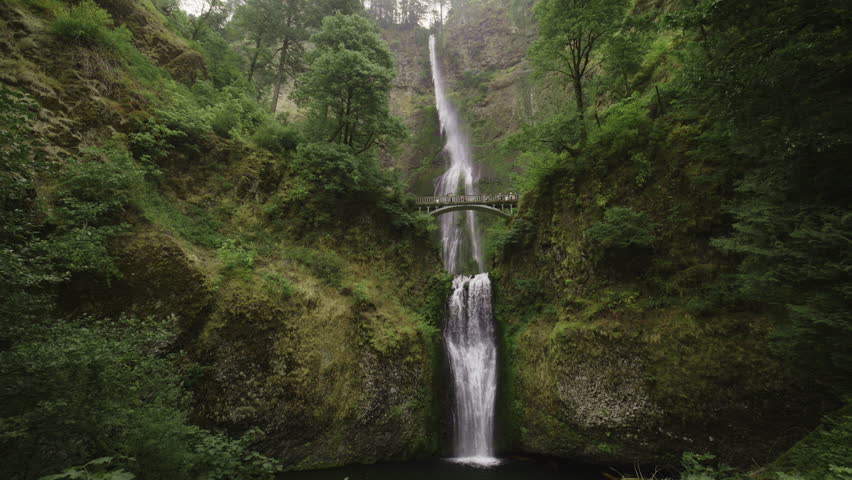 Panning shot of distant multnomah falls waterfall in green forest, bridal veil, oregon, united states
