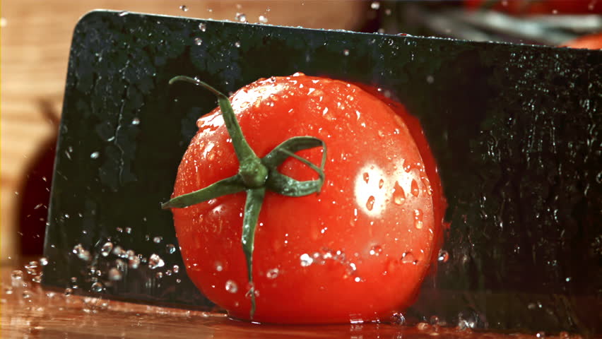 A knife cuts a tomato with splashes. Filmed on a high-speed camera at 1000 fps. High quality FullHD footage