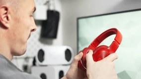A man is sitting in a comfortable office at home and wearing big red wireless headphones.