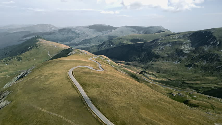 Sweeping view of the Transalpina roadway in Romania, with undulating terrains and contrasting landscapes under a cloudy sky.