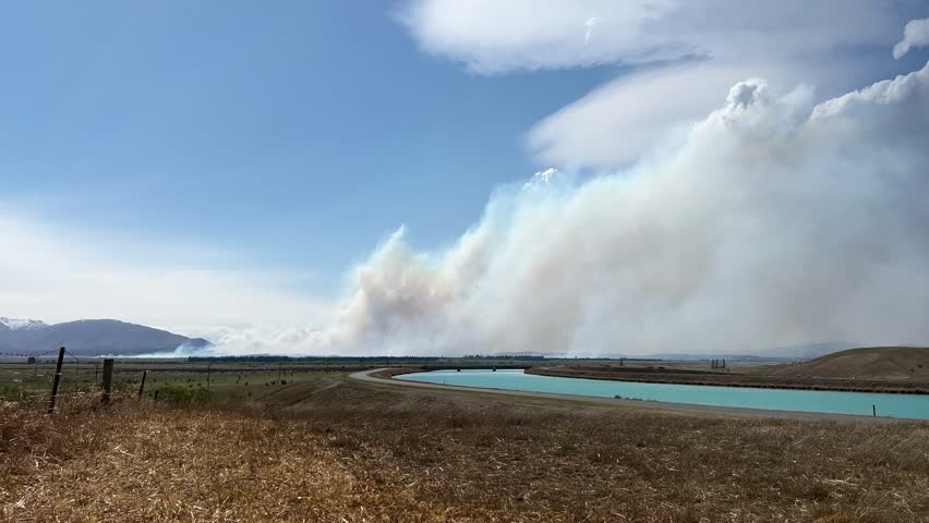 Massive amounts of smoke rising from 2023 Pukaki Downs scrub fire; turquoise hydro canal in foreground