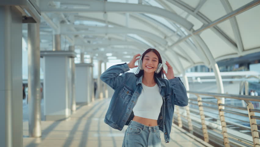 Happy young asian woman wearing headphones and enjoying music on the urban street city, Smiling female listening to music and dancing alone.
