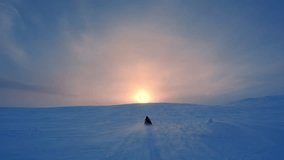 Snow mobile drive fast to the large low Sun in frosty cold foggy winter sky above mountain top in Norway. Drift snow, beautiful evening light, blue shadows. Scenic action camera video