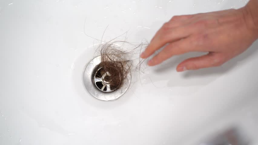 Cleaning the water drain in the sink from hair. A drain in the shower clogged with women's hair. The problem of hair loss and the problem of clogged plumbing. Clogged Drains. Royalty-Free Stock Footage #1110337825