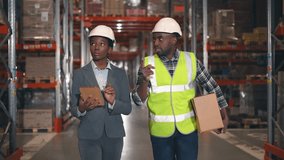 Two African American industrial workers walking along warehouse. Female manager holding tablet and making notes. Contractor gesturing and talking to supervisor consultant. - Powered by Shutterstock - Get 15% off with code: PIKWIZARD15