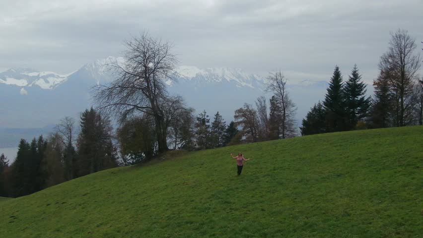 Cinematic aerial drone beautiful woman dancing Swiss Alps countryside dance jump in the fog hillside sounds of music scene Thun Bern Interlocken Switzerland mountainside circling slowly right movement