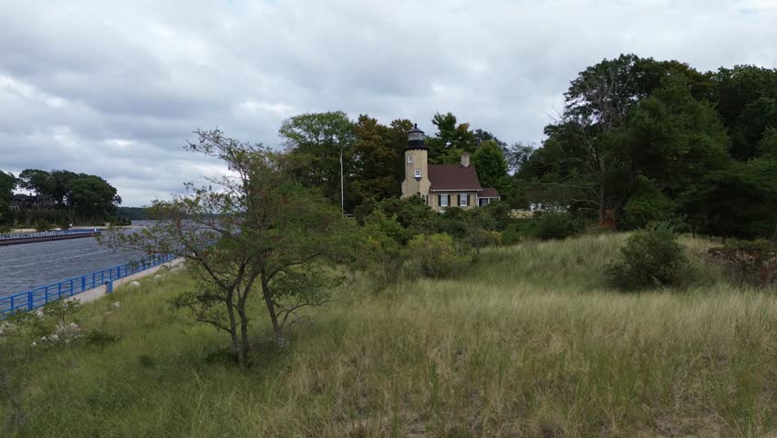 White River Lighthouse on Lake Michigan. Low aerial shot along the ship channel weaves through grasses, bushes and around trees as it slowly pushes in towards the light house.