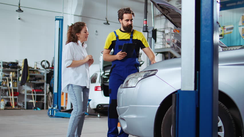 Mechanic listening to customer in auto repair shop, using tablet to write down car modifications she wants to make. Expert in garage with client, listening to her requests for vehicle tuning Royalty-Free Stock Footage #1110342573