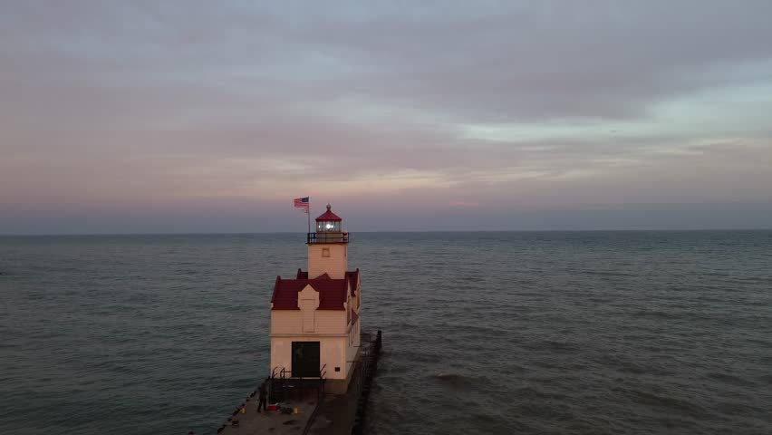 Kewaunee lighthouse on Lake Michigan. Aerial flyover shot, at light room level, along the pier from the shore towards the lake. Shot at dusk.
