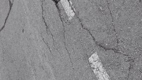 Vertical video, crack with deep faults on the road next to the white road markings, destruction highway due to natural disaster or improper operation, tracking shot.
