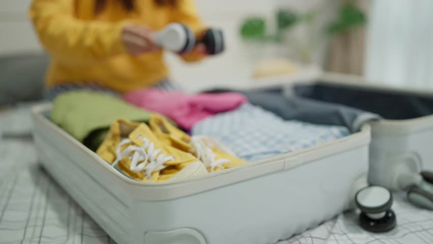 Woman traveller getting ready for travel and packing clothes in suitcase. Travel woman putting headphone and clothes in packing suitcase for vacation trip. Traveling and vacation concept Royalty-Free Stock Footage #1110344883