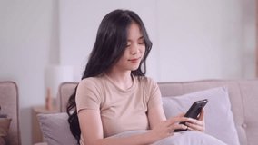young Asian woman hand holding smartphone sitting on the couch watching funny videos at home, Wireless communication and networking  concept 