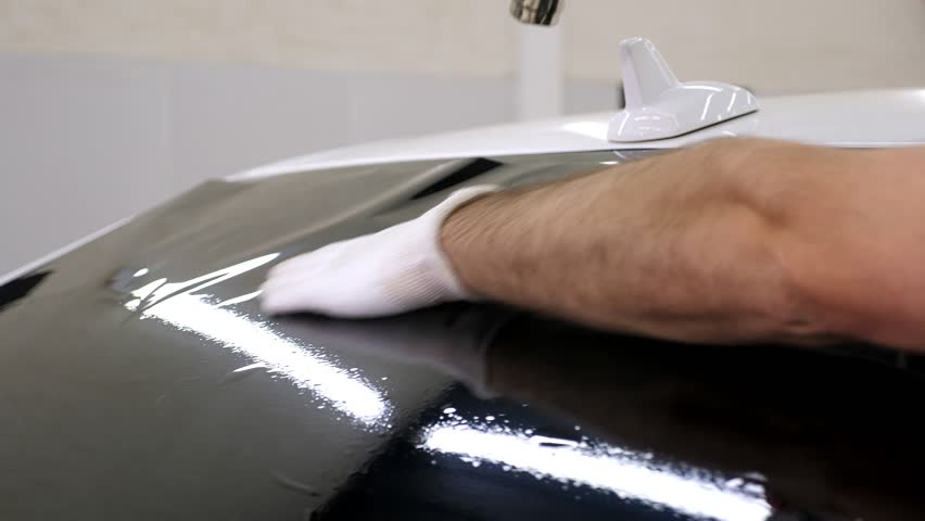 The master in gloves installs a tinting film on the car glass with a hair dryer and a spatula in bright light. Conceptual tinting of the car. Royalty-Free Stock Footage #1110347445