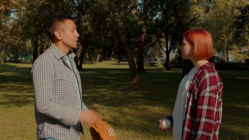 Cheerful lovely hearing impaired adolescent girl and handsome father with hearing loss wearing baseball gloves , celebrating successful baseball training, and fist bumping outdoors.