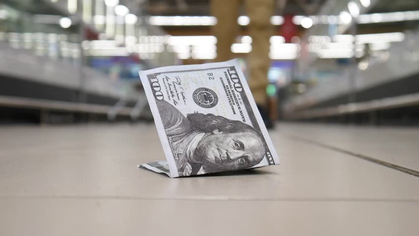 Close-up of a lost hundred dollar bill lying on the floor of a supermarket and a random man finds it