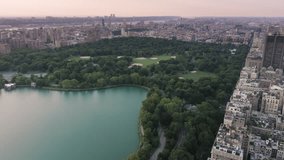 Beautiful lake surrounded by green park and buildings of Manhattan uptown in NYC. Cinematic Central Park 4K aerial of New York downtown. Green urban Central park, tourism background USA footage 