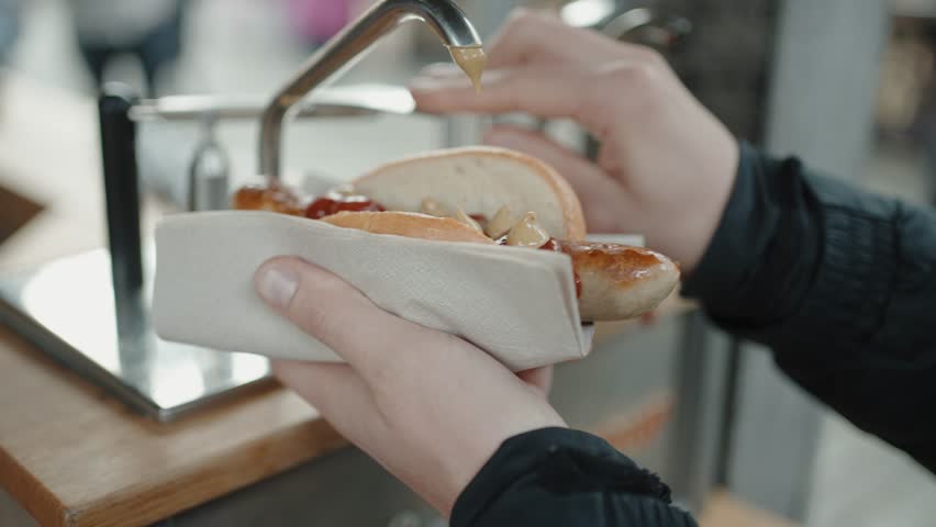 German bratwurst hot dog being drizzled with ketchup and mustard in a market