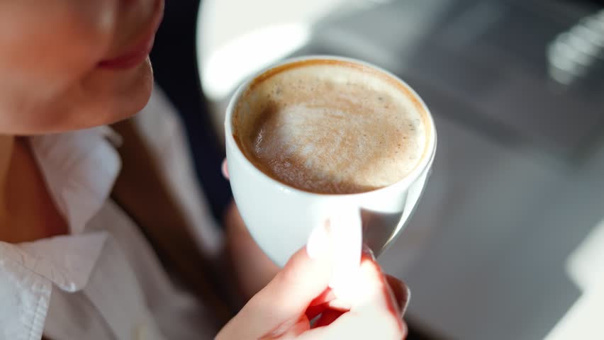Elegant businesswoman in professional attire gracefully cradles a fragrant cappuccino, savor breakfast in a sophisticated caffe or restaurant, hotel lobby during her business trip, tasty creamy latte.