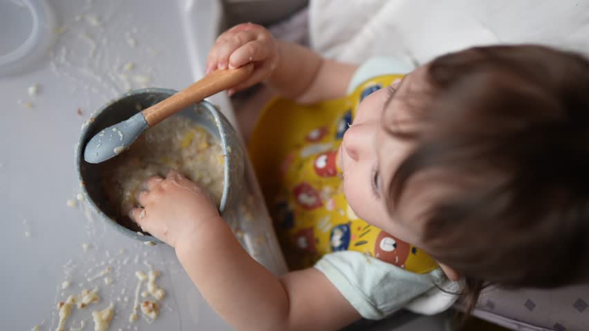 baby dirty eats. happy family toddler concept. baby girl learns to eat with her hands dirty her face dirty dream funny video dirty. baby on the table for feeding eats with her hands from cup Royalty-Free Stock Footage #1110357297